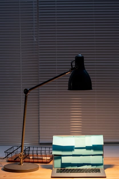 A close-up of an adjustable desk lamp illuminating a book and a notebook in a home office setting. The lamp provides focused, bright light.