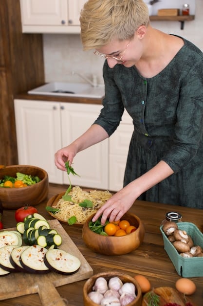 A person preparing a healthy meal in a well-lit kitchen. The focus is on the hands chopping vegetables on a cutting board, with a colorful array of fresh ingredients surrounding them. The scene conveys a sense of wellness and mindful food preparation.