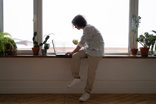 A person taking a short break at their home office, stepping away from the computer to stretch and look out the window, with natural light coming in.