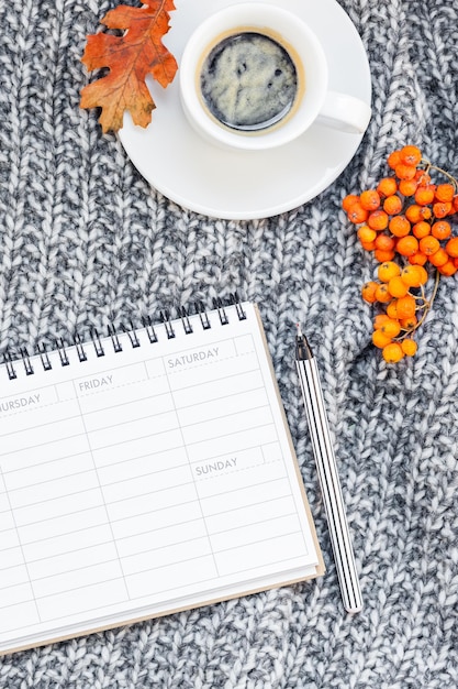 A close-up shot of a weekly planner showing time blocks scheduled for different tasks and appointments. The planner is lying on a wooden desk alongside a cup of coffee and a pen.