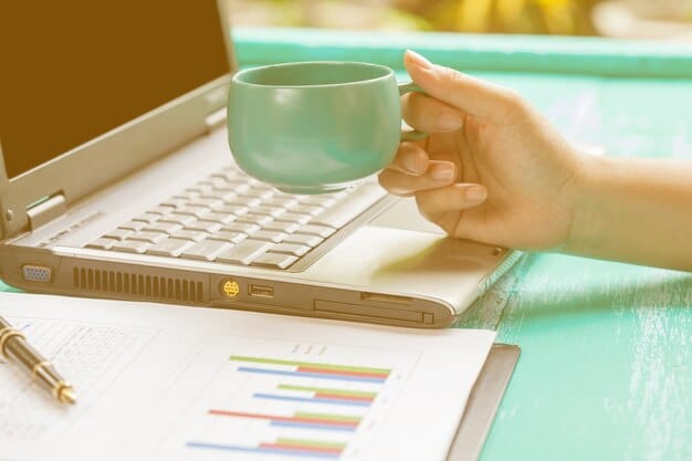 A close-up shot of a freelancer's hands typing on a laptop, with a spreadsheet showing income and expenses visible on the screen. A coffee cup and a small plant are in the background.